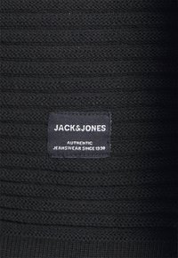 Czarna dzianina z poziomymi prążkami. Posiada prostokątną, tkana etykietę z napisem "JACK&JONES" oraz "AUTHENTIC JEANSWEAR SINCE 1990."