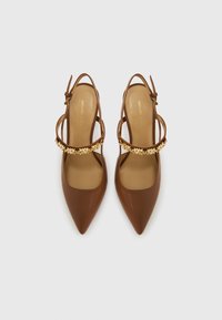 Talons en cuir brun à bout pointu avec une fine bride autour de la cheville, ornés d'un accent floral décoratif doré sur la bride. Texture lisse sur toute la surface.