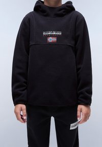 Černý fleece svetr s kapucí, zdobený vyšívaným logem a detaily norské vlajky na hrudi, v kombinaci s černými kalhotami.