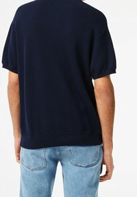 Chemise bleu marine à manches courtes avec texture côtelée et coupe droite. Portée avec un jean en denim clair, vue de dos.