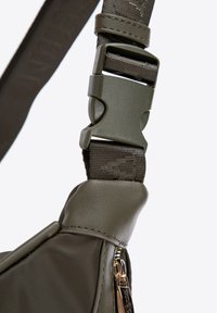 Cinghia verde in nylon con fibbia in plastica testurizzata e una cerniera in metallo, che mette in risalto una superficie liscia e un fissaggio sicuro.