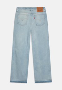 Jeans de mezclilla azul claro con un diseño de pierna recta, parche de cuero en la cinturilla y dos bolsillos traseros con detalle de costura curva.