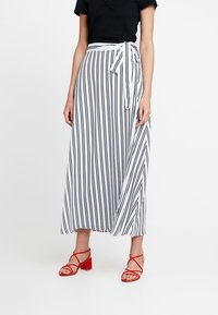 Black and white striped skirt with a flowing design, tie waist detail, and lightweight fabric, paired with red strappy sandals.