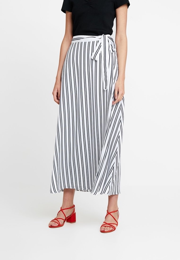 Black and white striped skirt with a flowing design, tie waist detail, and lightweight fabric, paired with red strappy sandals.