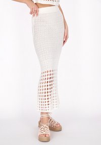 Vit stickad maxikjol med en åtsittande midja, med ett texturerat m�önster och öppen väv vid fållen; i kombination med beige espadriller med remmar.