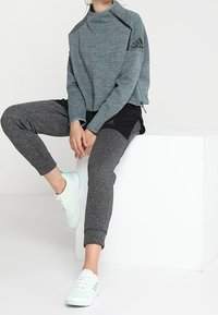 Pullover atletico grigio con colletto alto e accenti neri, abbinato a pantaloni jogger grigio scuro. Completato da sneakers verde chiaro.