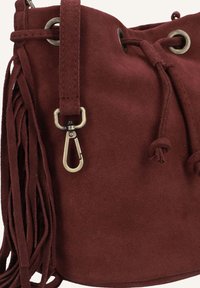 Bordeaux suède emmerse tas met een trekkoordsluiting, metalen oogjes en zijfranjes. Heeft een zilverkleurige metalen clipbevestiging.