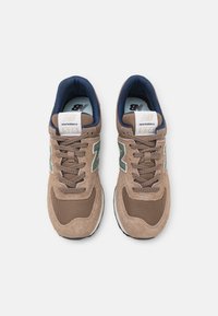 Tan mockasin- och mesh-sneakers med blåa detaljer, vita accenter och en grön logotyp. Utrustade med en vadderad tunga och texturerade sn ören.