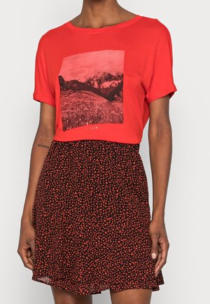 Czerwona bawełniana koszulka z nadrukiem góry, zestawiona z czarną spódnicą ozdobioną drobnymi czerwonymi serduszkami. Krótkie rękawy i luźny krój.
