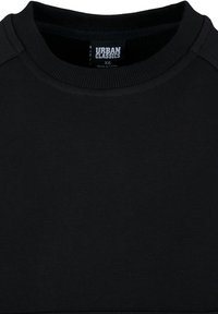 T-shirt noir col rond montrant un col côtelé et une étiquette de la marque Urban Classics avec la taille XS et le texte Made in China.