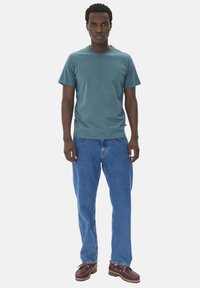 Camiseta de manga corta en color verde azulado combinada con jeans de pierna recta en color azul. Llevada con zapatos marrones de cordones que tienen una suela texturizada.
