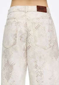 Jean en imprimé serpent beige avec une finition texturée, doté de deux poches arrière et d'une étiquette en cuir marron sur la ceinture marquée "BIMBA Y LOLA."