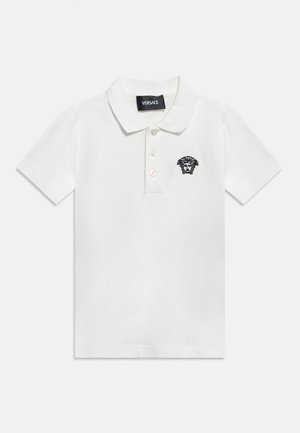 Tricou polo alb cu mâneci scurte, cu trei nasturi și logo negru Medusa pe partea stângă a pieptului, etichetă branduită Versace în interiorul gulerului.