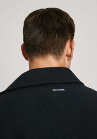 Melna vilnas maisījuma mēteli ar lielu apkakli, redzamām šuvēm un aizmugurējā etiķete ar uzrakstu "Pepe Jeans". Gluda tekstūra un piegriezums.