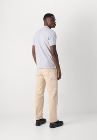 Lys grå polo t-shirt med korte ærmer, parret med beige cargo-bukser med flere lommer og sorte sneakers.