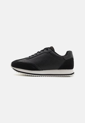 Black athletic shoes with a textured upper, suede accents, and a white midsole. Features a rounded toe and lace-up closure. Rubber outsole with traction.