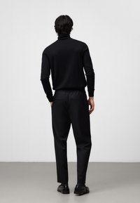 Czarny sweter w golf z dopasowanym fasonem, w połączeniu z czarnymi spodniami z elastycznym pasem i tylnymi kieszeniami. Całość dopełniają czarne buty.