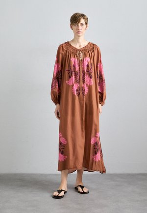 Brown, flowy dress with large pink floral patterns, round neckline, and gathered detail. Long sleeves taper at the wrists. Worn with black sandals.
