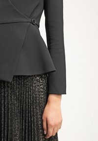 Blazer noir ajusté avec détail de boutons sur le côté, associé à une jupe plissée noire avec imprimé animalier métallique.