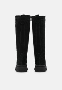 Botas altas de ante negro con una textura suave, que cuentan con un cierre de cremallera, costuras en contraste y una suela de goma gruesa.