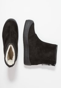 Bottines en daim noir avec une semelle en caoutchouc texturé, dotées d'une doublure douce blanche et d'une fermeture éclair apparente sur le côté.