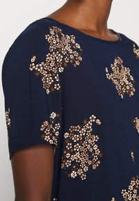 Top azul-marinho de manga curta com embellishments florais em branco e dourado, apresentando um decote redondo e uma textura de tecido suave.