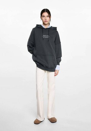 Mörkgrå oversize hoodie med en framficka, dragsko-capuchong och tryckt text. I kombination med off-white utsvängda byxor och bruna tofflor.