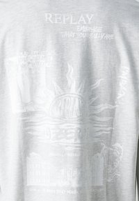 Camiseta de algodón gris con estampados gráficos blancos, incluyendo un diseño de sol y elementos de texto. Corte relajado con una textura suave.