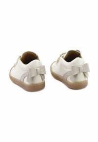 Zapatos de cuero blancos con suelas marrón claro, con un diseño texturizado y un pequeño lazo en la parte trasera. Acabado suave y bajo perfil.