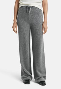 Woman wearing high-waisted, wide-leg gray knit pants with a drawstring, paired with black shoes and a tucked-in white top.