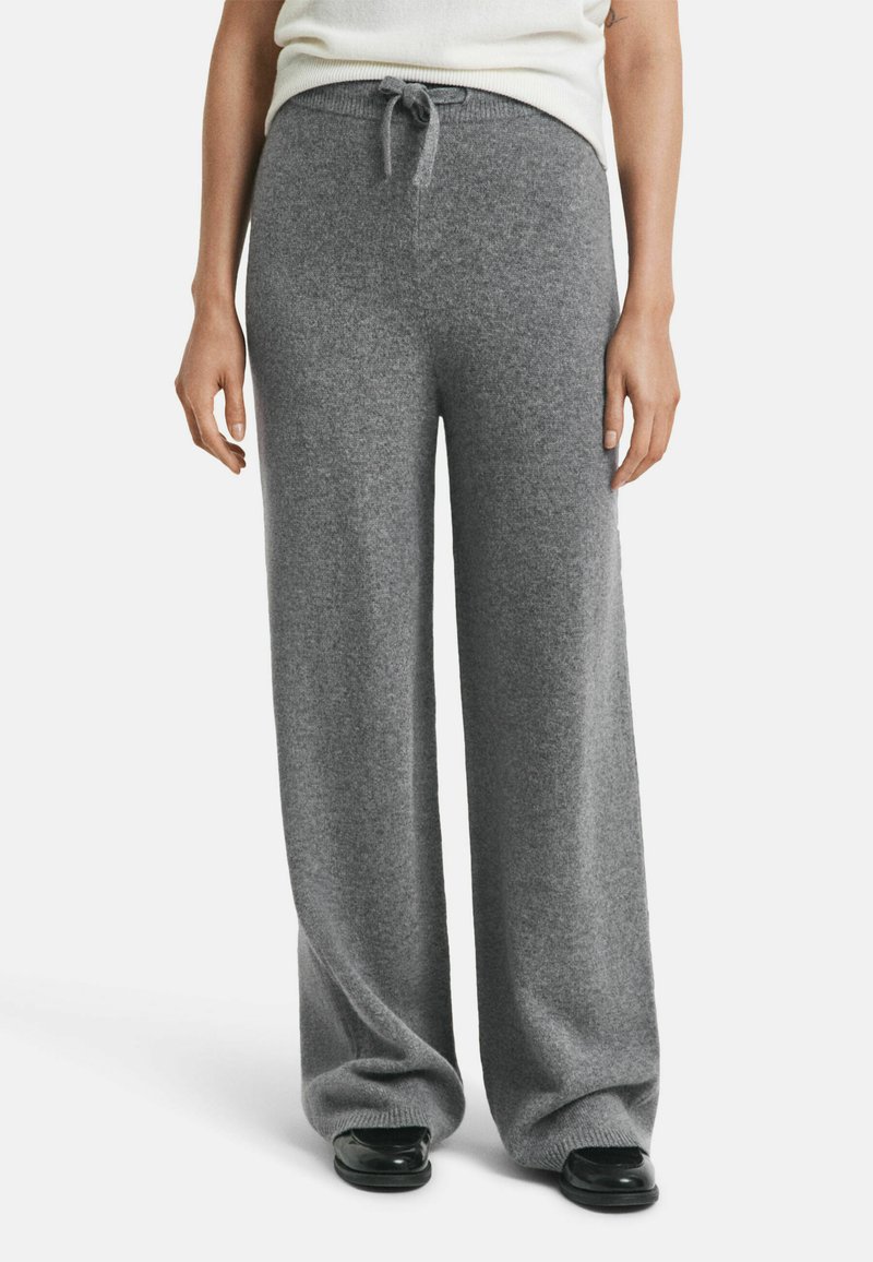 Woman wearing high-waisted, wide-leg gray knit pants with a drawstring, paired with black shoes and a tucked-in white top.