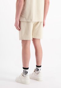 Crème-kleurige katoenen shorts met een losse pasvorm, gecombineerd met witte sneakers en zwarte accenten op de sokken. Eenvoudig ontwerp, minimale details.