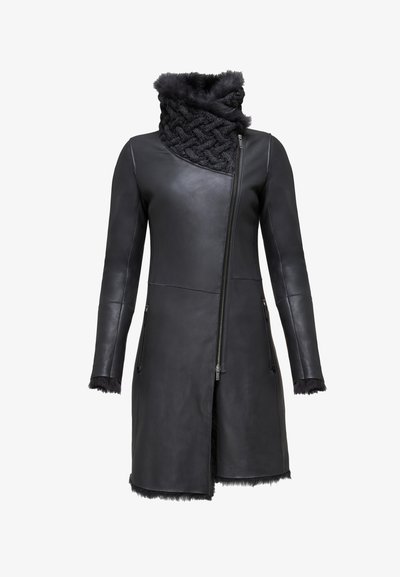 Crni kožni kaput s asimetričnim zatvaranjem na munjac, teksturiranim krznim ovratnikom i krznom na rubovima rukava i donjem rubu. Elegantnog je, prilagođenog dizajna.