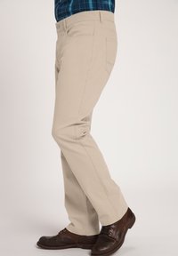 Pantalones beiges de mezcla de algodón, con un diseño de pierna recta, bolsillos frontales y un cierre de botón en la cintura. Se ven zapatos marrones.