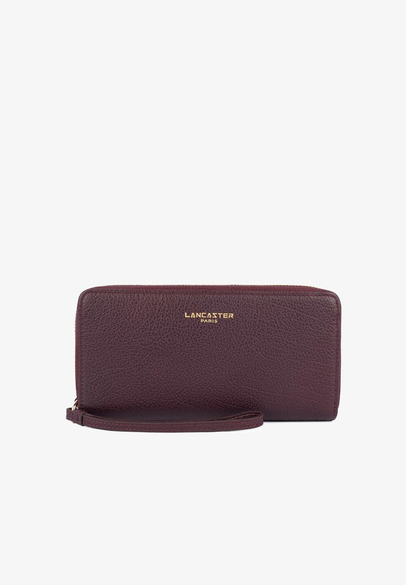 Portefeuille bracelet en cuir texturé violet foncé avec logo doré Lancaster Paris et fermeture éclair en haut sur fond blanc.