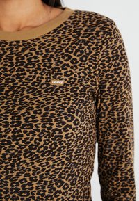 Levi's košulja dugih rukava u smešnoj boji s crnim uzorkom leoparda. Ima rebrasti tekstur i malu logotip oznaku na prsima.