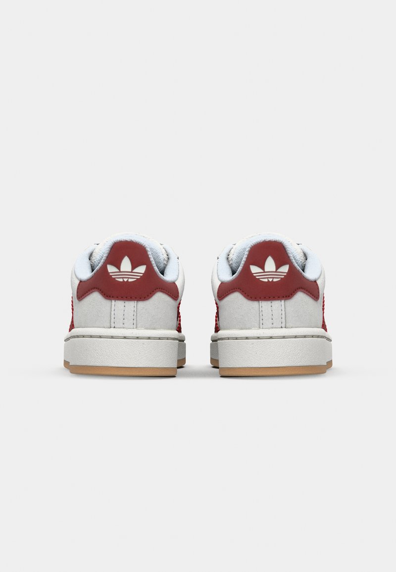 Weiße Sneakers mit roten Akzenten, strukturiertem Wildleder, Leder-Hinterstück, Gummisohle und Logodetail auf der Rückseite. Minimalistisches Design.