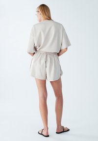Lichtbeige, kortingen top met verlaagde schouders, gecombineerd met bijpassende shorts met een elastische tailleband en zijsplitten. Verder een gladde textuur.