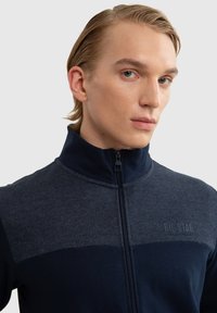 Mornarska zip-up jakna s dvobojnim dizajnom, glatkom teksturom, visokim ovratnikom i urezanom logotipom "BIG STAR" na prsima.