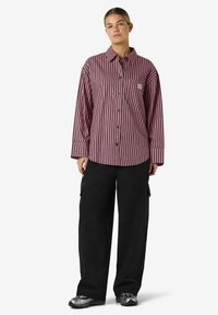 Rød og rosa langermet skjorte med striper, krage og lomme, kombinert med svarte vide cargobukser og metalliske joggesko.