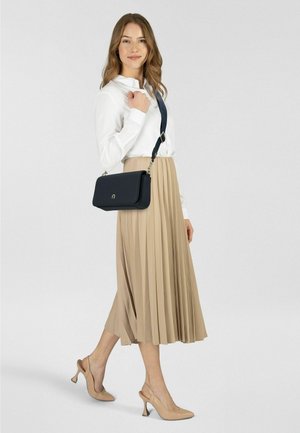 Eine schwarze Leder-Umhängetasche mit glatter Oberfläche, silbernen Beschlägen und abnehmbarem Riemen; kombiniert mit einem plissierten beigen Rock und nudefarbenen High Heels.