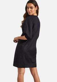 Zwarte jurk met driekwartmouwen, ronde halslijn, zijzakken en een iets losse pasvorm. Gemaakt van lichtgewicht stof met een gladde textuur.