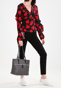 Sort bluse med rødt rosenmotiv, flæset ærmer; sorte bukser; grå tekstureret tote bag med hvid lynlås; hvide sneakers.