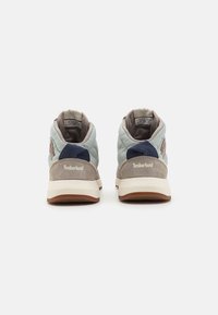 Two Timberland sneakers in grey and light blue. Feature a padded design, textured suede and fabric, and a rubber sole. Brand name displayed on heel.