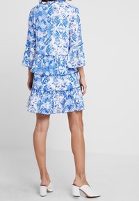 Vestido floral azul y blanco con volantes en capas, mangas largas de campana y tela estampada, combinado con mule blancos de tacón.