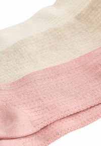 Trois sections de tissu côtelé dans des couleurs crème, beige et rose clair. La texture est douce, avec des variations notables dans les motifs de tricot.