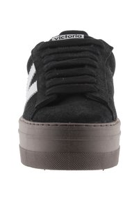 Zapatillas de fieltro negras con puntera redonda, con una suela gruesa de goma marrón y franjas laterales blancas. Los cordones y una lengüeta con marca completan el diseño.