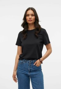 Schwarzes Baumwoll-T-Shirt mit Rundhalsausschnitt, kurzen Ärmeln und entspannter Passform, kombiniert mit hochtaillierten blauen Jeans und einem strukturierten Armband.