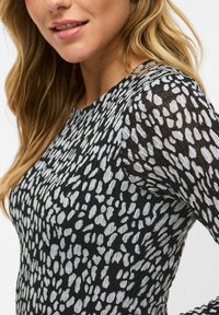 Haut noir avec un motif abstrait blanc. Fabriqué en tissu léger avec des manches longues et transparentes et un col rond. Design ajusté.