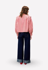 Gestreepte rode en witte cropped jas met pofmouwen, gecombineerd met hoog-gesneden donkere spijkerbroeken met een wijde pijp en contrasterende manchetten.